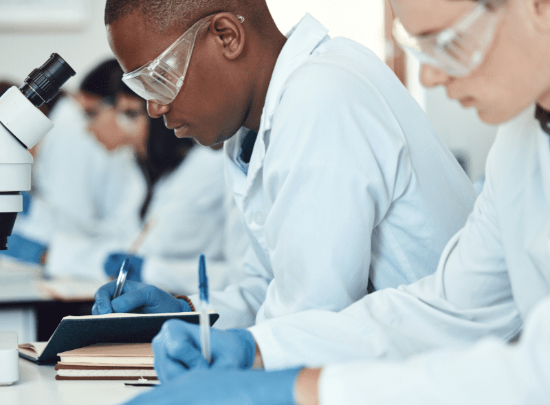 Divi images for overlapping text & image modules 800 x 598 pixelspx (2) A photo of a man and woman wearing googles in a lab writing things down in a notebook.