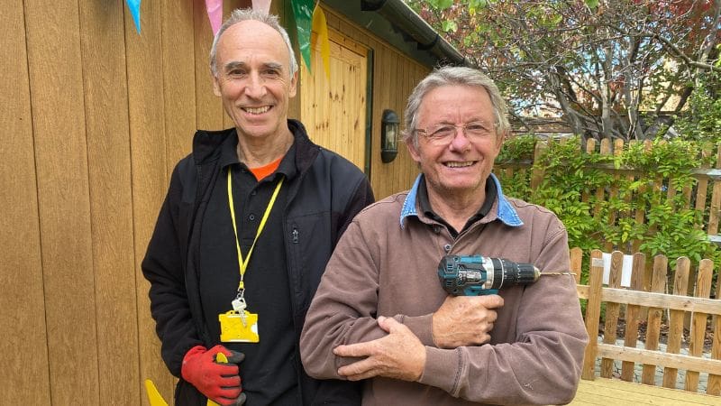 Stewart and Phil Stewart and Phil, Estates volunteers for Helen & Douglas House are standing in the Hospice garden. Phil is holding a drill.