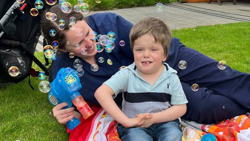 Jasper and a nurse sitting and playing with bubbles in the Helen & Douglas House garden.