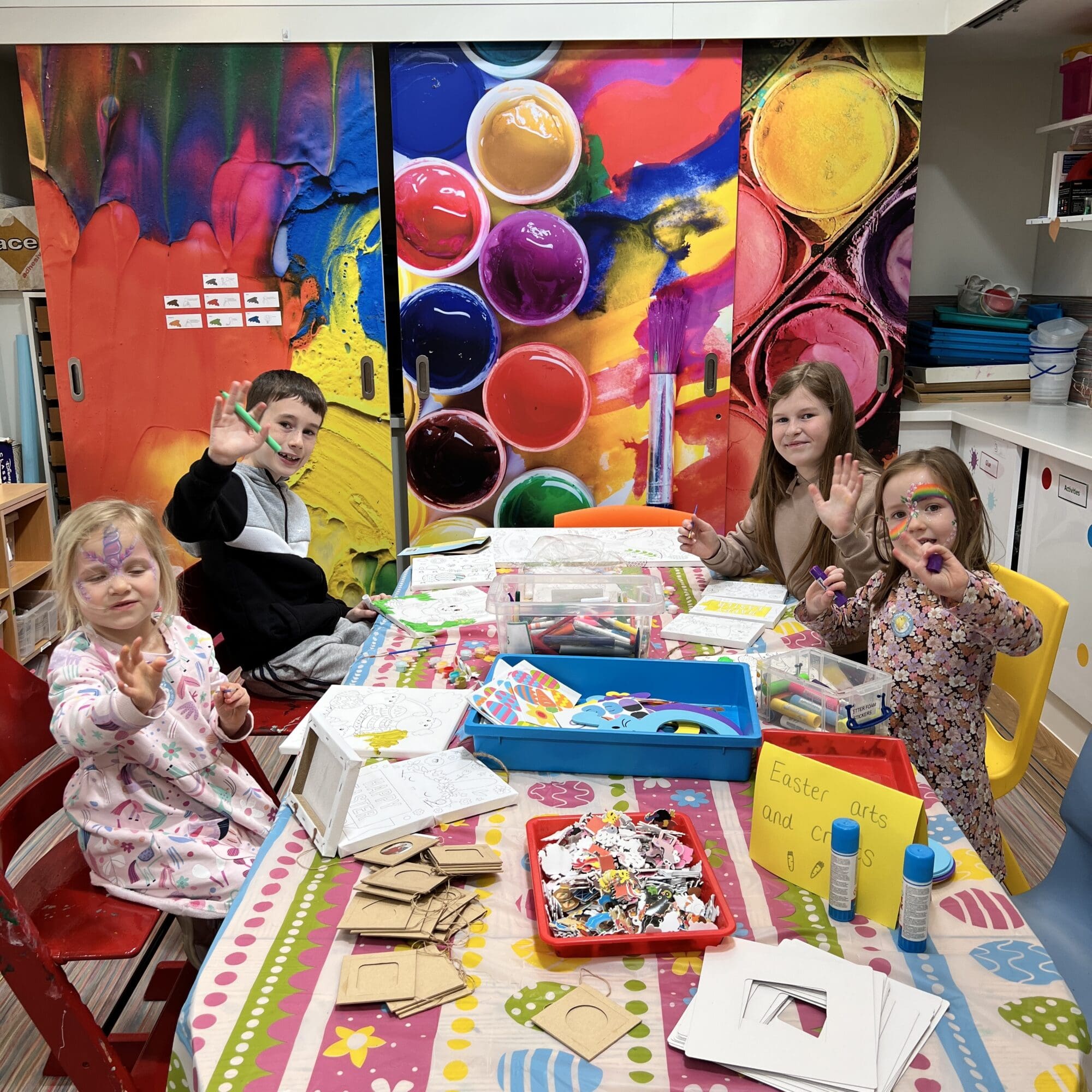 4 children sat at the table crafting easter biscuits and smiling at the camera