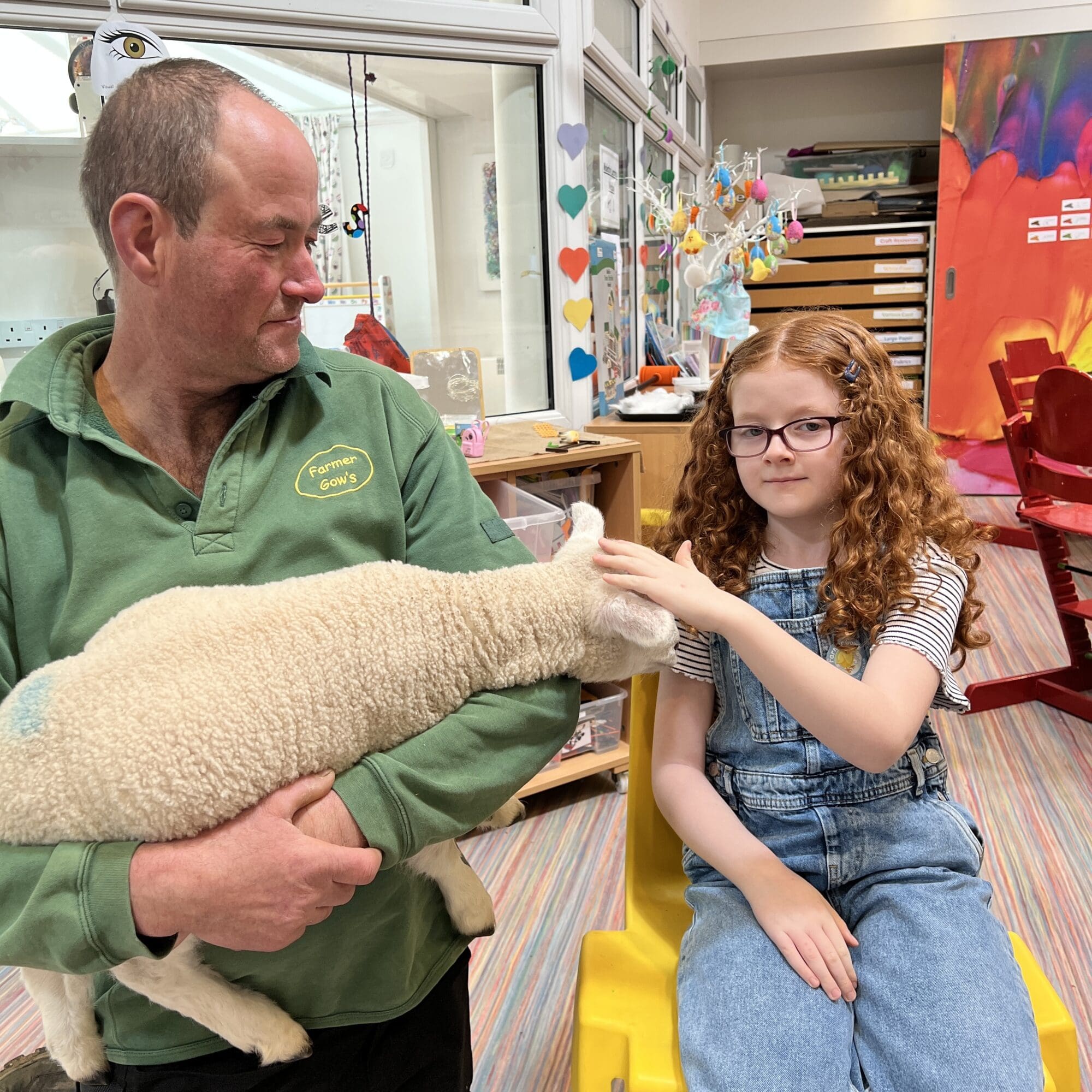 Farmer holding a lamb next to a girl with ginger hair