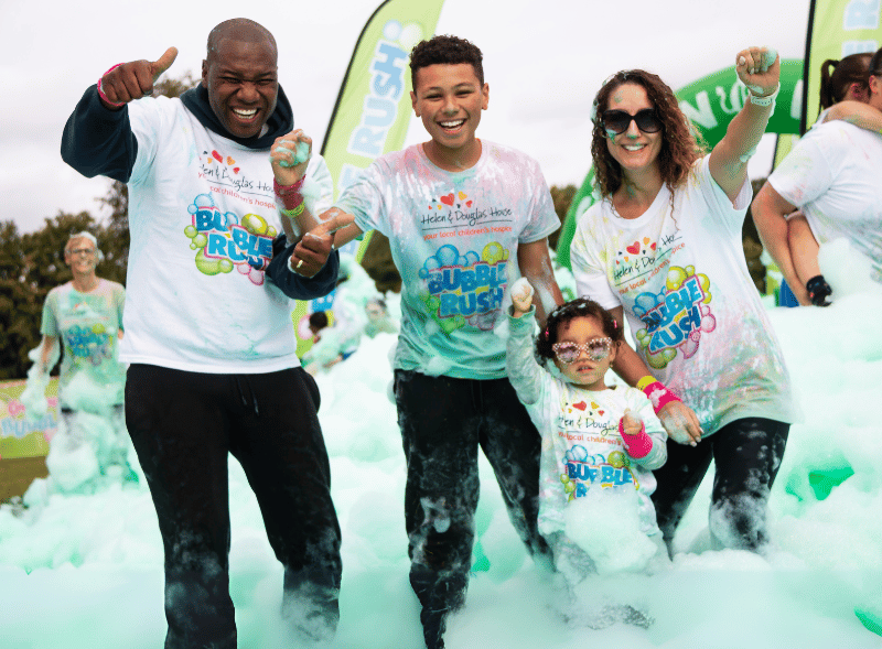 Bubble Rush Photos A mum, dad, teenage boy and young girl holding hands and cheering. They are standing in knee high green bubbles.